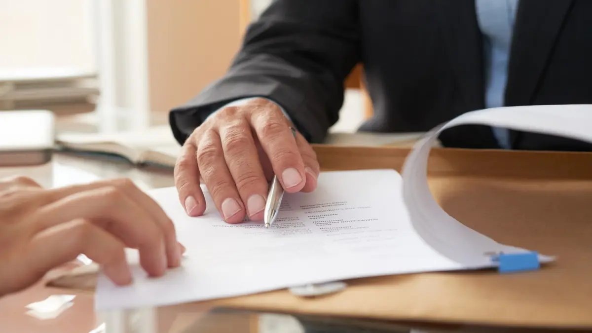 Close-up of businessman examining business contract and signing it at the office desk