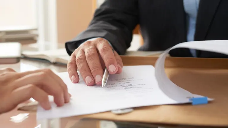 Close-up of businessman examining business contract and signing it at the office desk